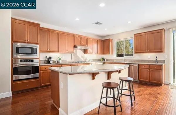 a kitchen with stainless steel appliances granite countertop a stove top oven a sink dishwasher and a refrigerator with wooden floor