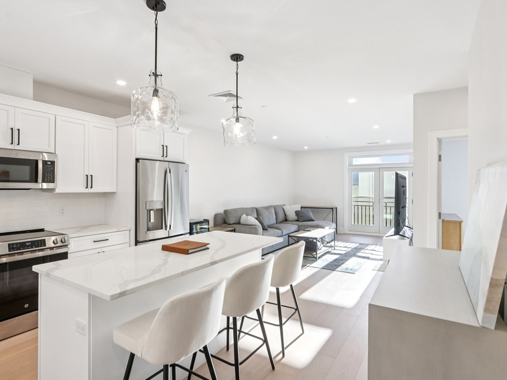 62 Foundry Street, Unit 204 Wakefield, MA 01880 - Photo 11 of 28 a kitchen with stainless steel appliances kitchen island granite countertop a dining table chairs refrigerator and sink