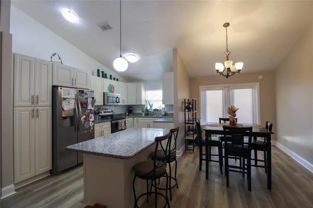 a kitchen with stainless steel appliances granite countertop a dining table chairs stove refrigerator and microwave