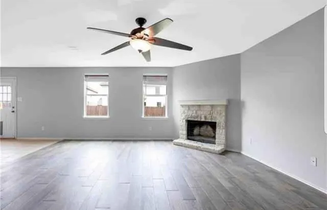 a view of an empty room with wooden floor fireplace and a window
