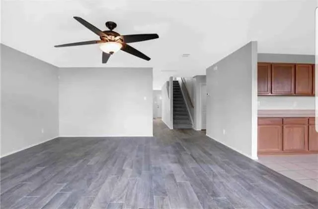 a view of an empty room with wooden floor and a ceiling fan