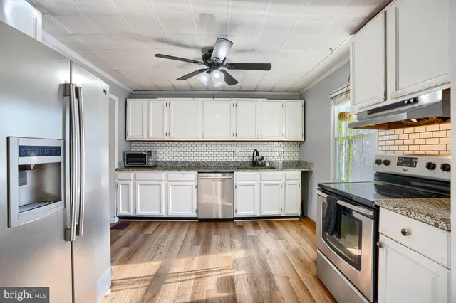 a kitchen with granite countertop a refrigerator a sink and white cabinets