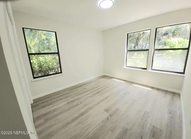 a view of an empty room with wooden floor and a window