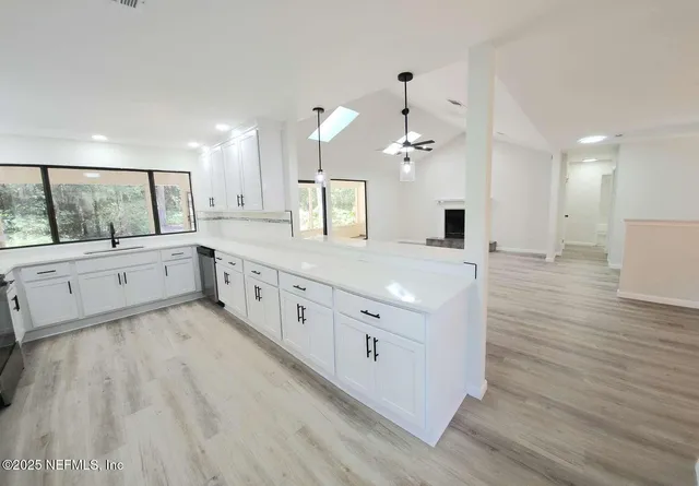 a large white kitchen with a large island wooden floor and stainless steel appliances
