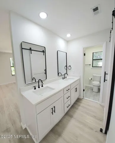 a spacious bathroom with double vanity sink a mirror and a toilet
