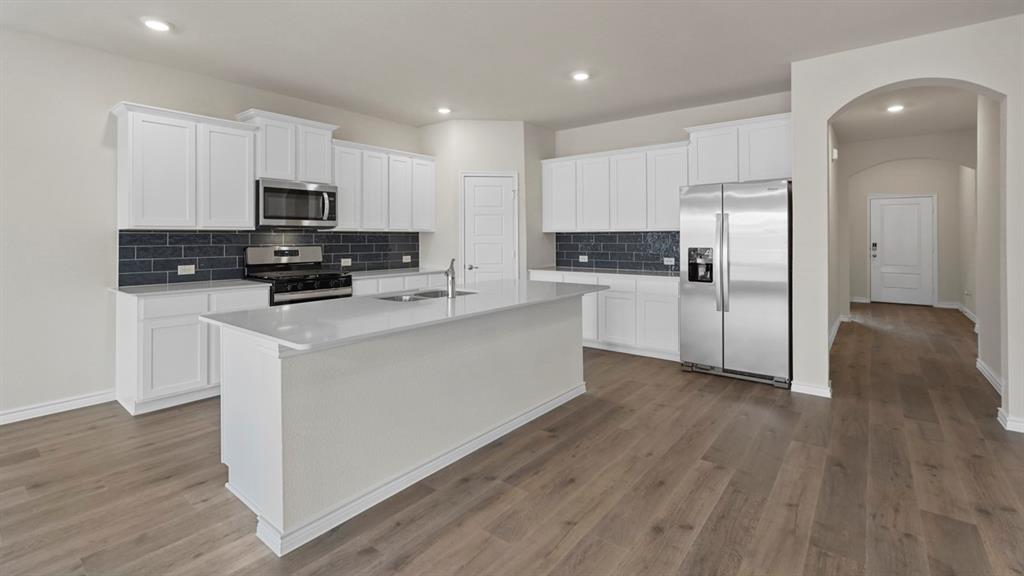 447 Epiphany Lane Lavon, TX 75166 - Photo 4 of 31 Modern kitchen featuring a central island with an undermount sink, white cabinetry, stainless steel appliances, and wood-finish flooring