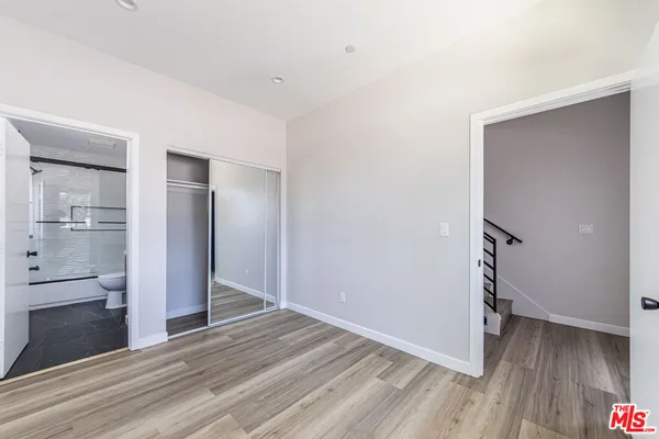 a view of empty room with wooden floor and kitchen