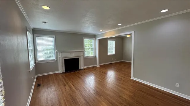 an empty room with wooden floor fireplace and windows