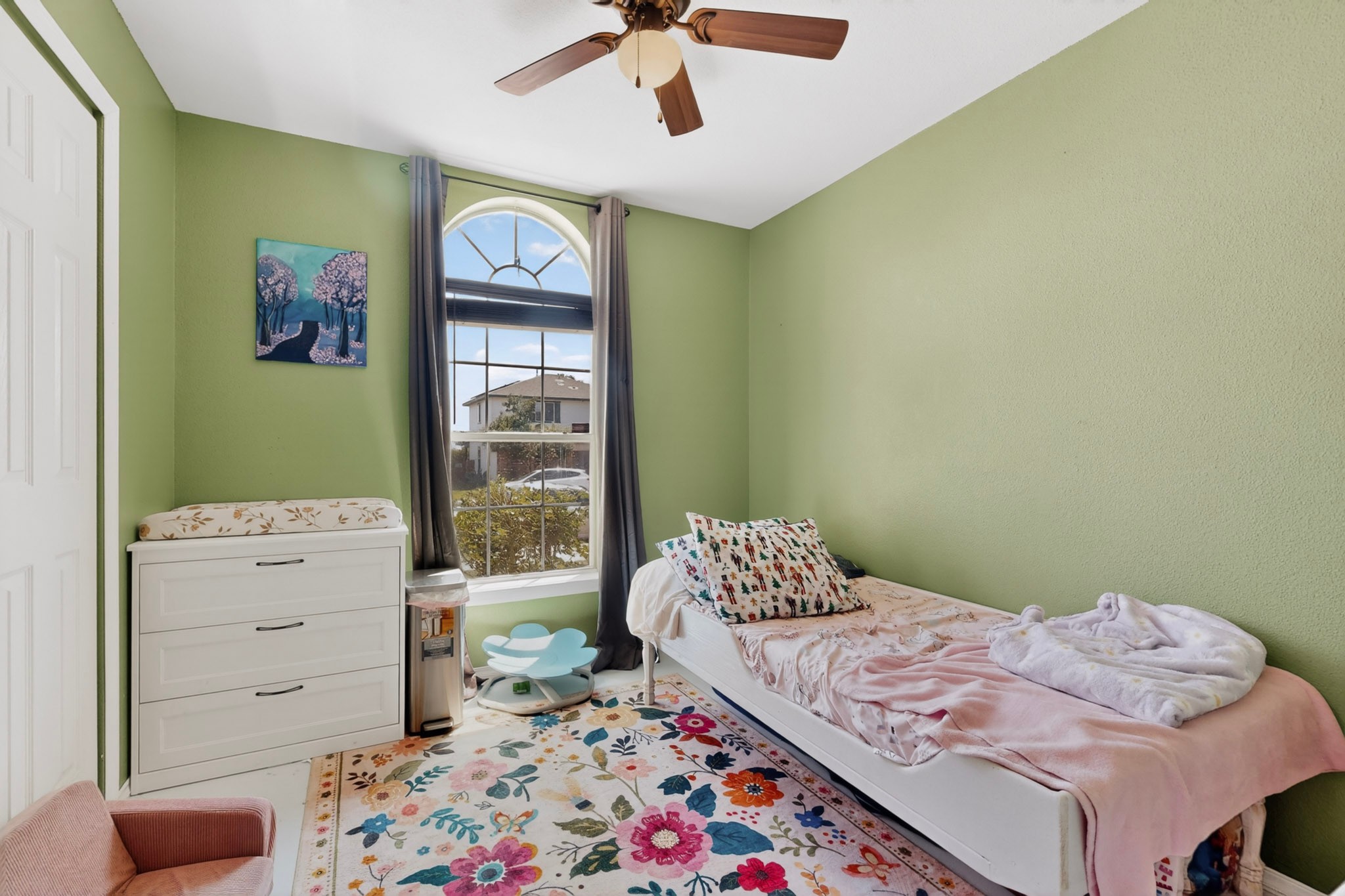 15104 Mimebark Way Austin, TX 78724 - Photo 24 of 38 Bedroom featuring a large arched window with dark drapery, green textured walls, and a ceiling fan