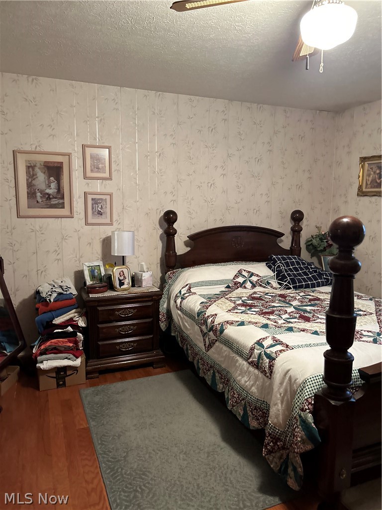73323 Old Twenty One Road Kimbolton, OH 43749 - Photo 8 of 14 Bedroom with a textured ceiling, wood finished floors, wallpapered walls, and ceiling fan