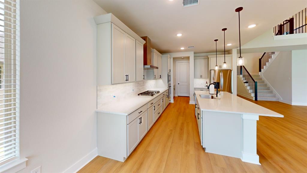 2708 Andesite Road McKinney, TX 75071 - Photo 10 of 35 Open-concept kitchen with light wood-finish flooring, white cabinetry, a large kitchen island with pendant lighting, stainless steel appliances, and a gas range