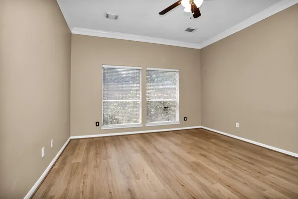 an empty room with wooden floor chandelier fan and windows