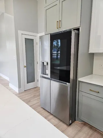 a view of a refrigerator in kitchen and an empty room with wooden floor