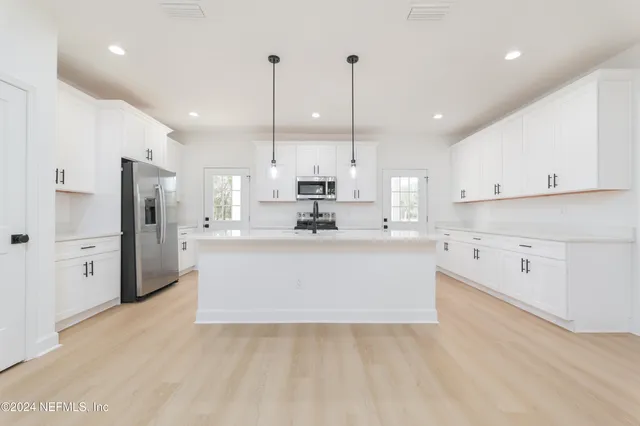 a large white kitchen with a large window a refrigerator and white cabinets