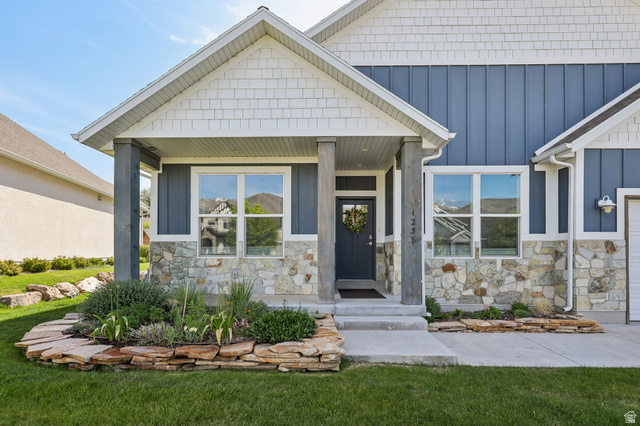 Front exterior featuring a covered porch with stone pillars, board and batten siding, horizontal shingle accents, and a stone facade