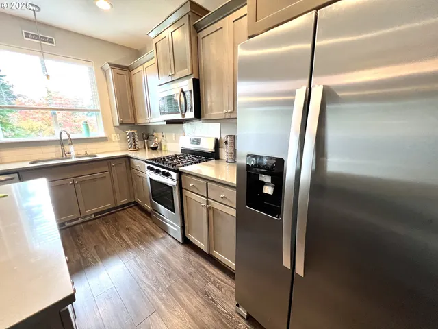 a kitchen with stainless steel appliances granite countertop a refrigerator a sink dishwasher a stove and white countertops with wooden floor