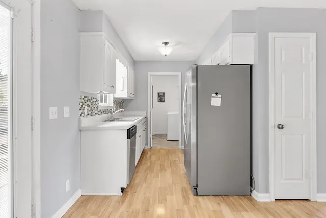 a kitchen with a sink dishwasher and white cabinets with wooden floor