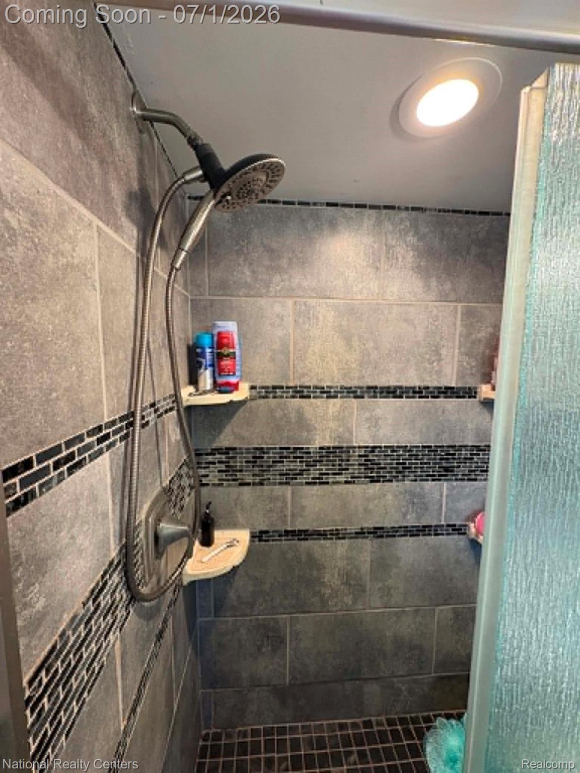 1330 Brauer Road Oxford, MI 48371 - Photo 42 of 54 Shower enclosure featuring large format gray wall tiling, black mosaic tile accent bands, dual corner shelving, a handheld shower fixture, and a recessed ceiling light