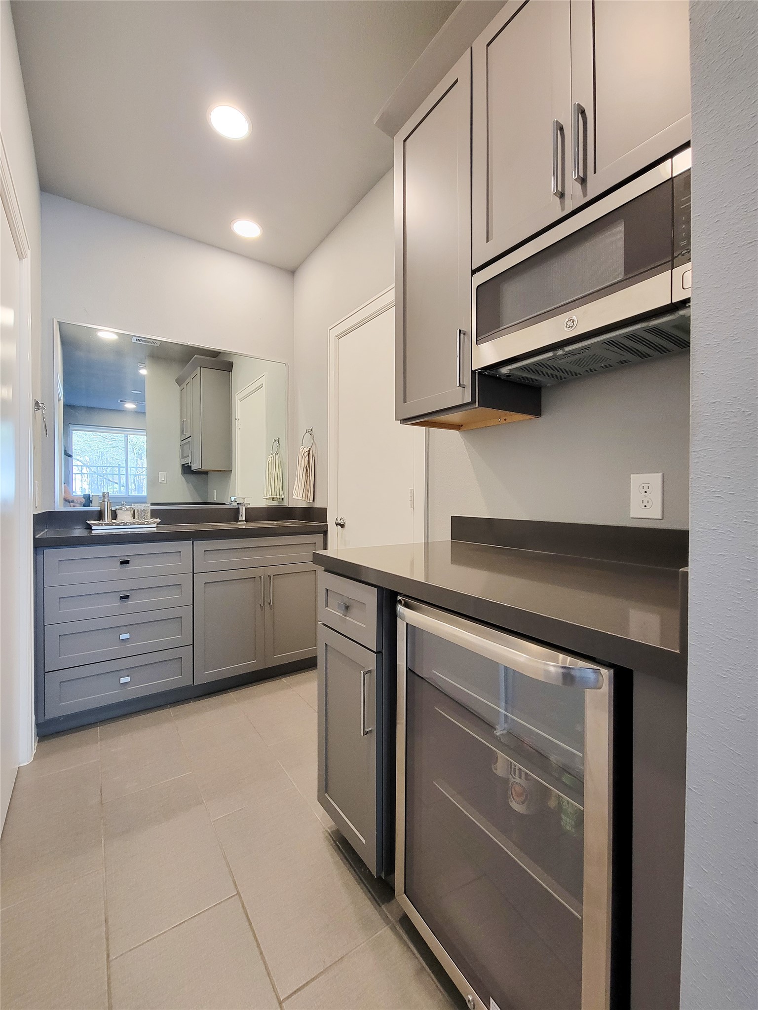 1705 Eado Point Lane Houston, TX 77003 - Photo 10 of 50 1st Floor Bedroom includes a modern kitchenette with sleek gray cabinetry, a built-in microwave, and a wine fridge. The space features ample storage, a large mirror, and recessed lighting, creating a bright and functional area.