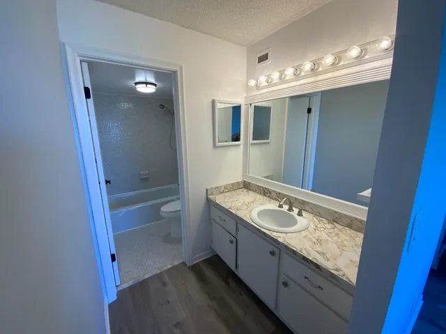 a bathroom with a granite countertop sink a toilet a mirror and shower