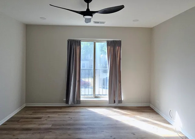 an empty room with wooden floor fan and windows