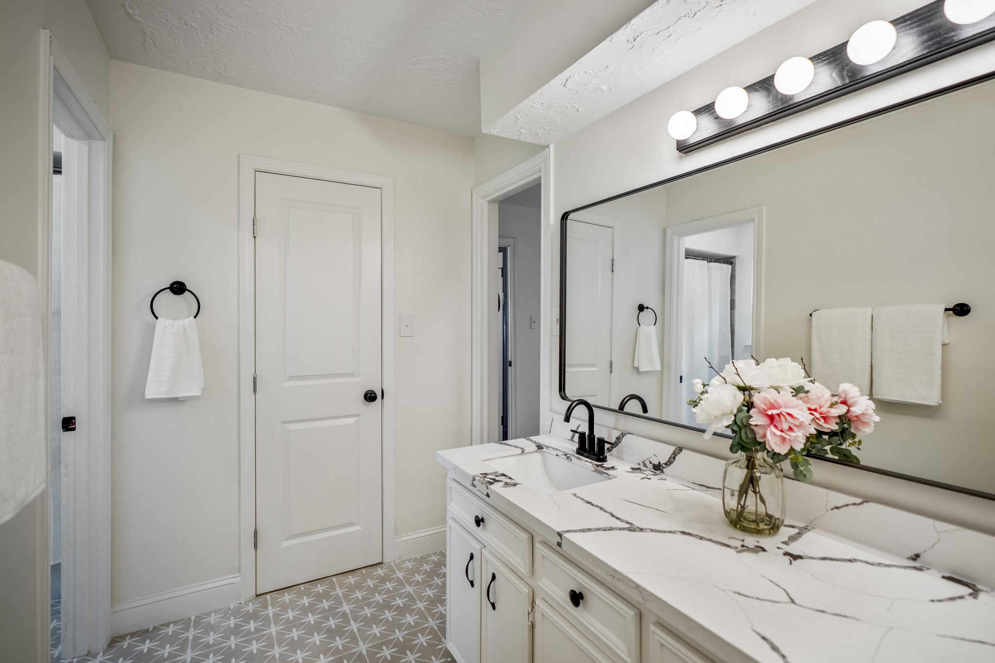 6303 Larkmount Drive Spring, TX 77389 - Photo 25 of 50 From here, the ensuite’s practical layout becomes even clearer, with one walk-in closet tucked behind the closed door and the vanity continuing along the right side. Updated tile flooring, refreshed finishes, and a bright vanity area keep the bathroom feeling clean and functional while still connected to the primary suite’s calm, refreshed feel.