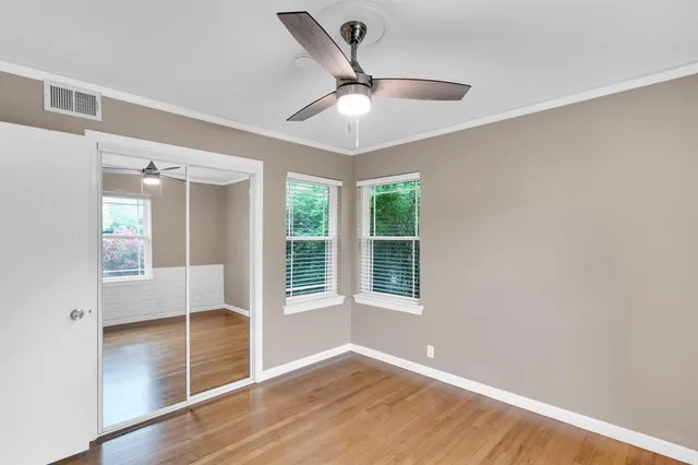 an empty room with wooden floor fan and windows