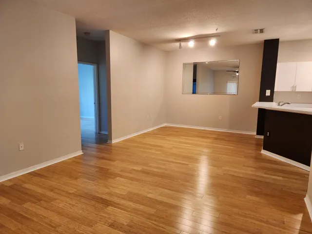 a view of an empty room with wooden floor and a mirror