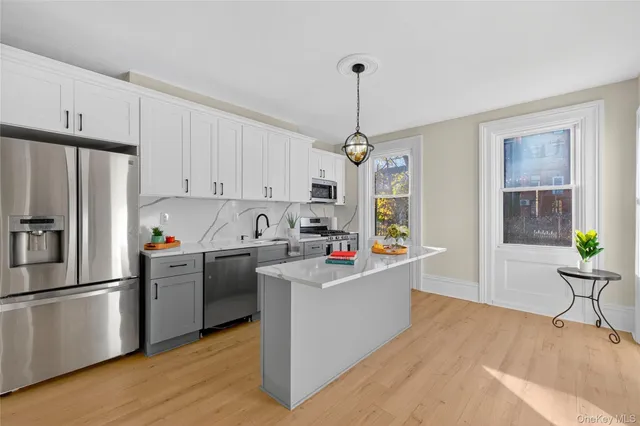 a kitchen with stainless steel appliances kitchen island a refrigerator a stove a sink dishwasher a oven with white cabinets and wooden floor