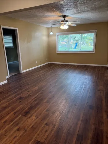an empty room with wooden floor chandelier fan and windows