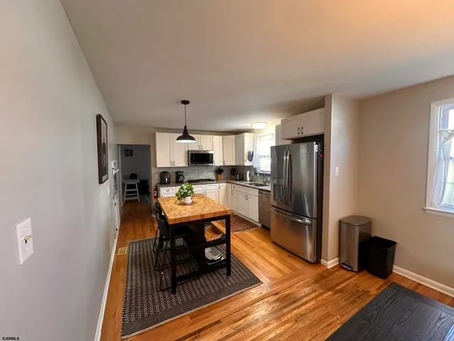 a living room with stainless steel appliances a dining table wooden floor and a window