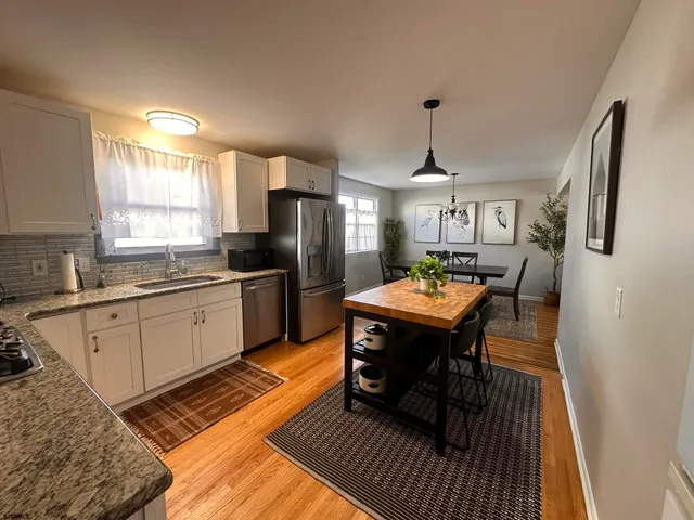 a kitchen with granite countertop a refrigerator a sink dishwasher a stove and white cabinets with wooden floor