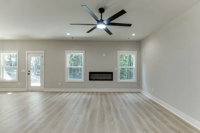 an empty room with wooden floor a ceiling fan and windows