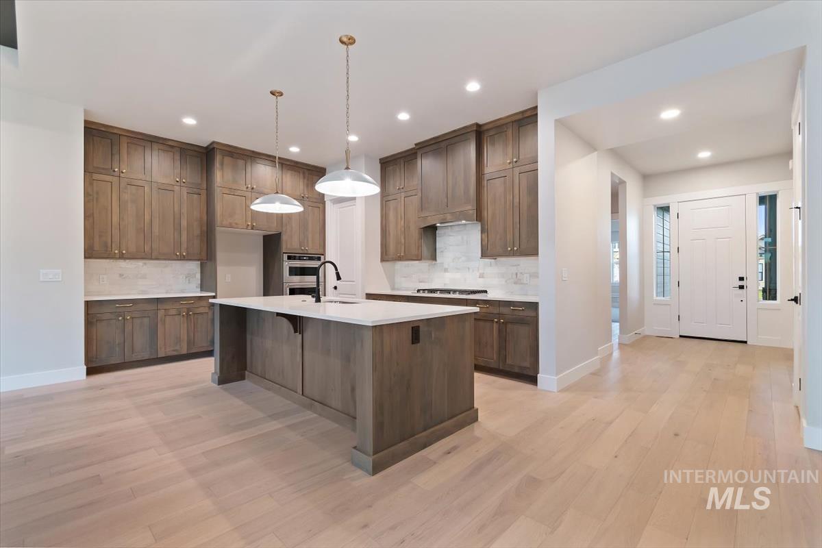 2147 East Blakehurst Avenue Kuna, ID 83634 - Photo 9 of 43 Kitchen featuring hanging light fixtures, a breakfast bar, light wood-style flooring, an island with sink, and backsplash