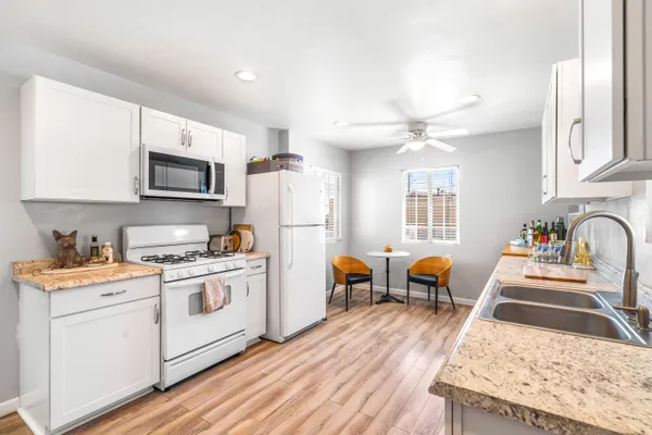 a kitchen with stainless steel appliances granite countertop a stove top oven a refrigerator a sink dishwasher a dining table and chairs with wooden floor