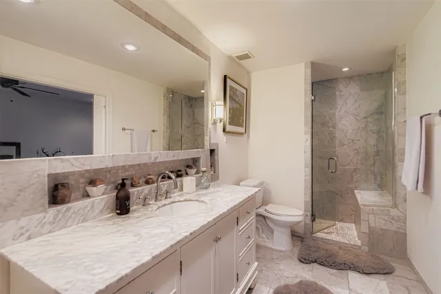 a bathroom with a granite countertop sink a toilet a mirror and shower
