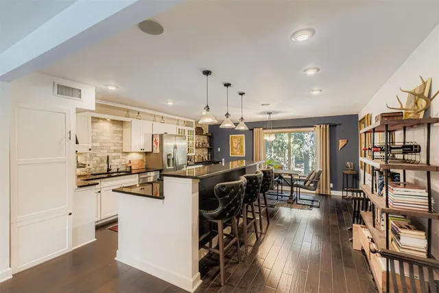 a kitchen with stainless steel appliances kitchen island granite countertop a stove a refrigerator a dining table and chairs with wooden floor