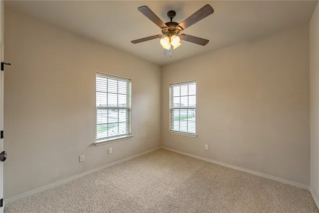 an empty room with chandelier fan and windows
