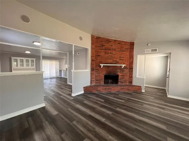 a view of an empty room with wooden floor fireplace and a window
