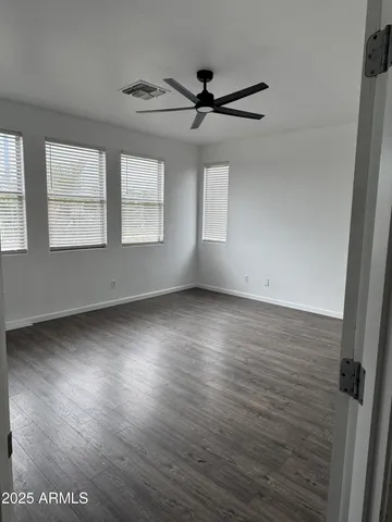 an empty room with wooden floor fan and windows