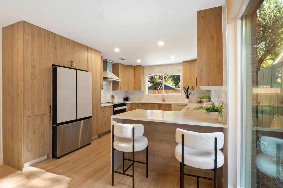 7010 Meadow Run Austin, TX 78745 - Photo 4 of 26 Kitchen with modern cabinets, a peninsula, freestanding refrigerator, a kitchen breakfast bar, and light stone countertops