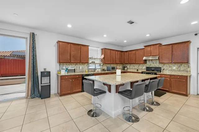 a kitchen with stainless steel appliances granite countertop a stove top oven a sink a dining table and chairs