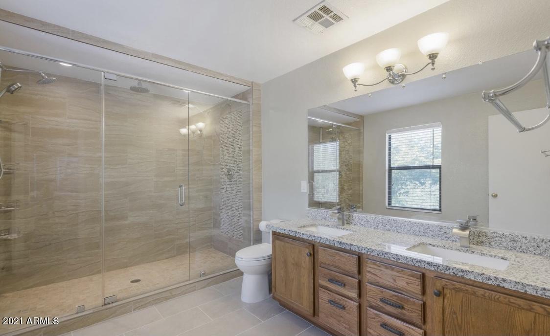 9446 Virginia Avenue Phoenix, AZ 85037 - Photo 12 of 19 a bathroom with a granite countertop double vanity sink a toilet a mirror and shower