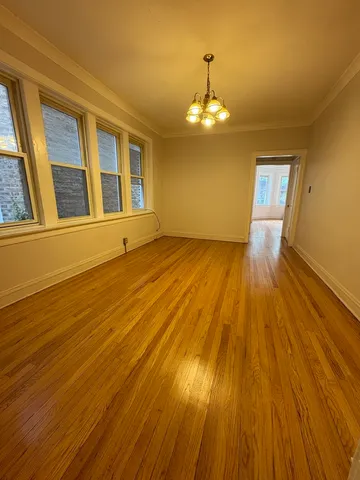 a view of an empty room with wooden floor and chandelier