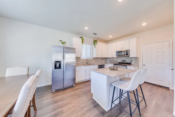 a kitchen with stainless steel appliances a refrigerator a stove a sink dishwasher and a dining table with wooden floor
