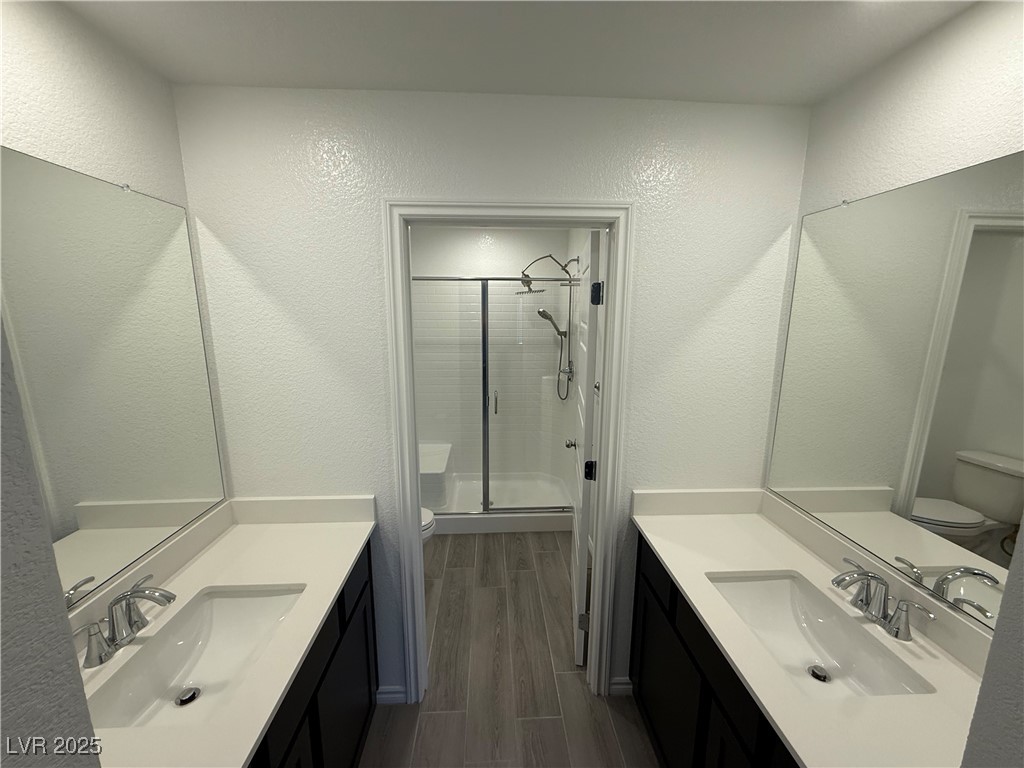 10774 Astell Isle Court Las Vegas, NV 89166 - Photo 21 of 34 Bathroom with a shower stall, wood finish floors, a textured wall, and two vanities