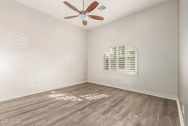 an empty room with wooden floor fan and windows