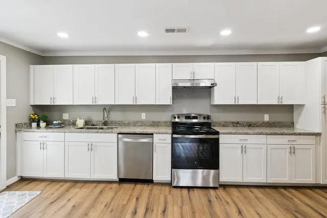 a kitchen with stainless steel appliances granite countertop a stove a sink and white cabinets