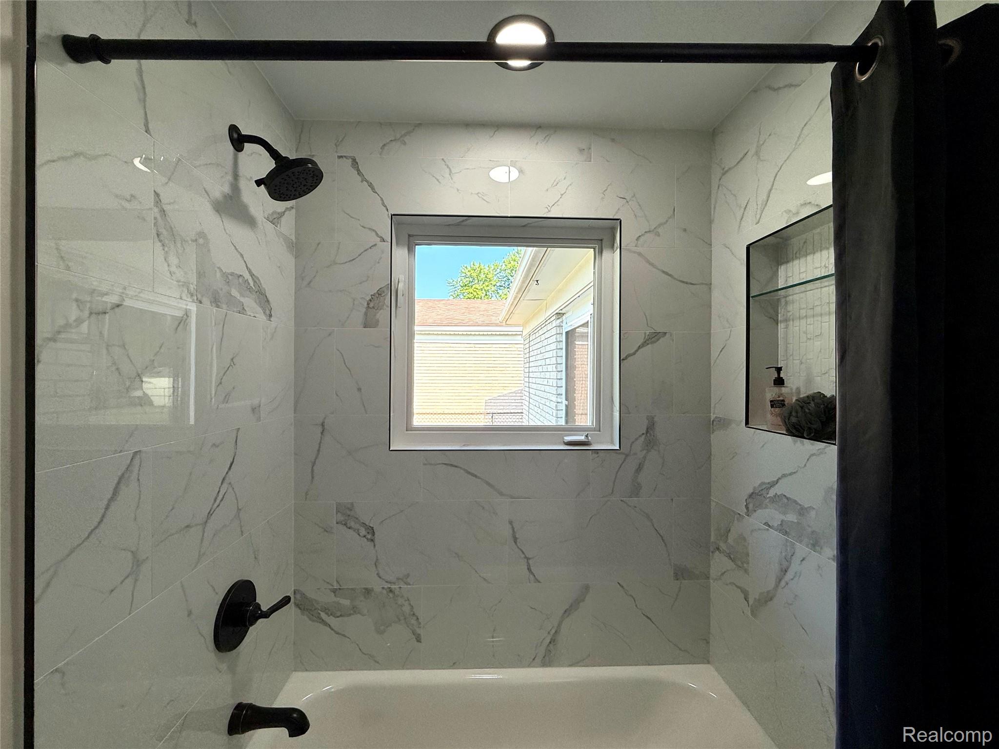 39909 Lynn Street Canton, MI 48187 - Photo 17 of 45 Bathtub and shower combination featuring white marble-look tile, matte black fixtures, a recessed window, and a built-in shower niche with glass shelving