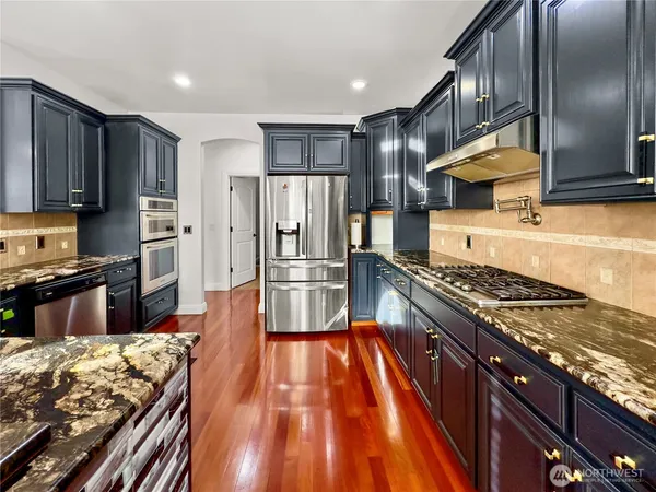 a kitchen with stainless steel appliances granite countertop a stove top oven a sink dishwasher a refrigerator and cabinets with wooden floor